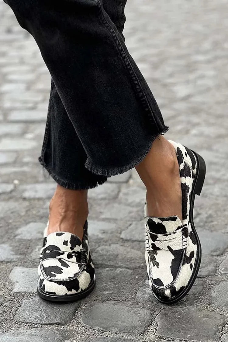 White and black cow print loafers with round toes and low heels