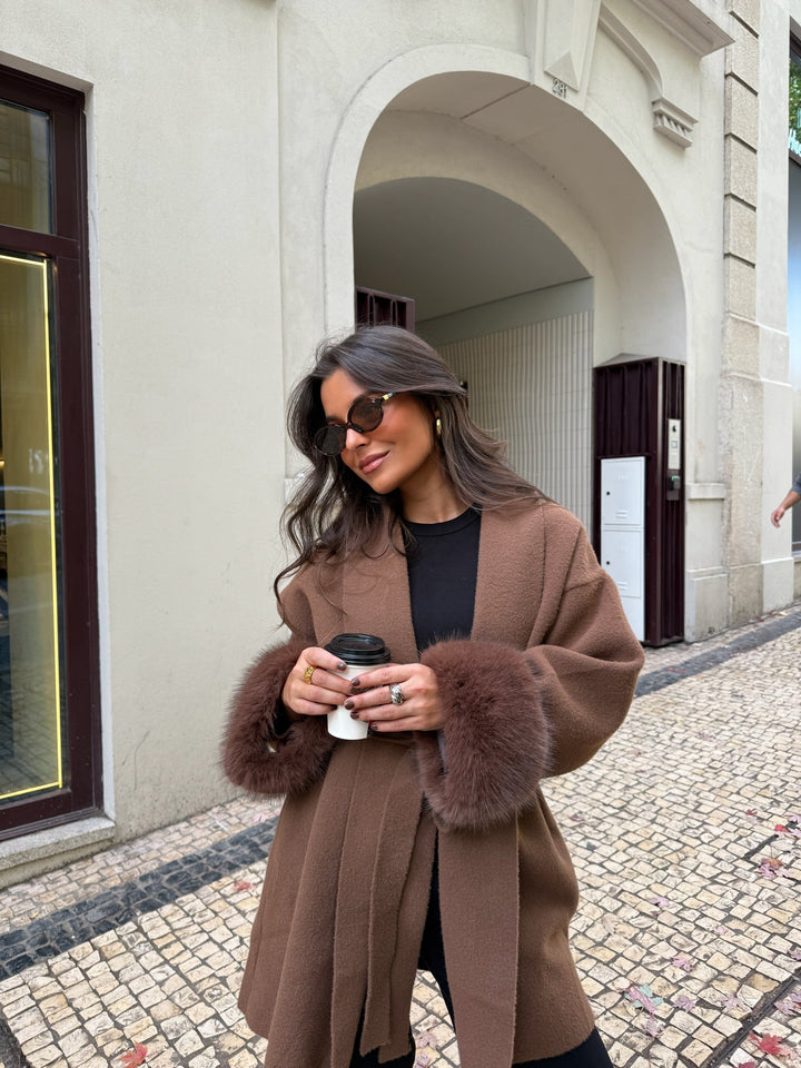 Woman wearing a brown long coat with fur-trimmed cuffs and tie belt